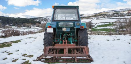 Ein alter Traktor mit Arbeitsgerät parkt inmitten einer schneebedeckten Wiese. Berglandwirtschaftliches Konzept