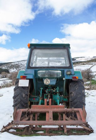 Vieux tracteur équipé d'outils stationnés au milieu d'une prairie enneigée. Concept d'agriculture de montagne