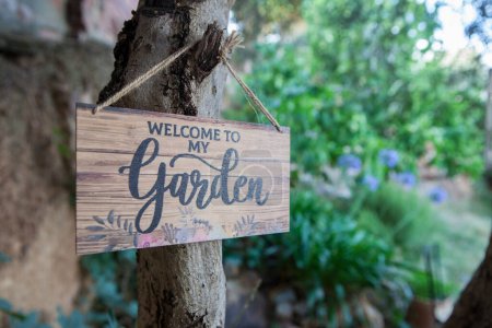 Señal de bienvenida al jardín con patio mediterráneo como fondo. Letras en inglés