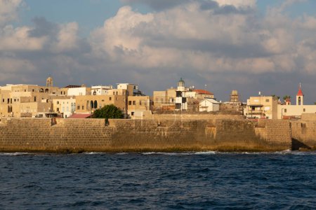 Foto de Vista desde el mar a la antigua ciudad de Akko con una muralla de fortaleza, un faro, una iglesia y edificios residenciales en ruinas - Imagen libre de derechos