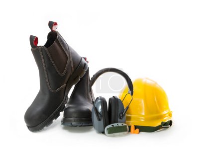 Foto de Work boots, earmuffs from the noise at the enterprise and a yellow hard hat on a white background - Imagen libre de derechos