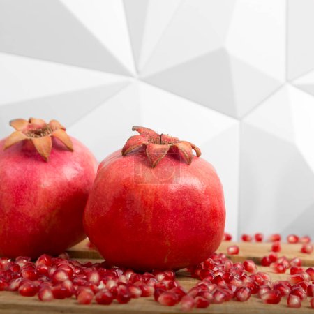 Foto de Two whole pomegranates and red seeds scattered randomly on a wooden table - Imagen libre de derechos