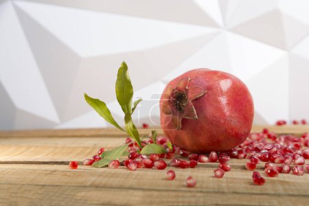 Foto de Red pomegranate with a sprig of green leaves and juicy seeds scattered on a wooden table - Imagen libre de derechos