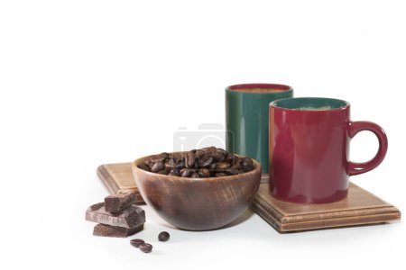 Foto de Granos de café aromáticos asados en un tazón de madera, trozos de chocolate y dos tazas sobre un fondo blanco - Imagen libre de derechos