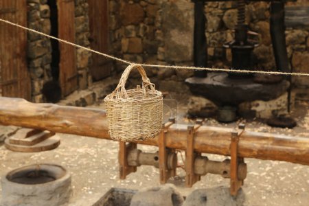 Foto de Cesta de mimbre hecha de ramitas suspendidas en una cuerda en un antiguo molino de aceite de oliva - Imagen libre de derechos