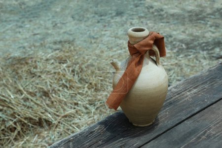 Foto de Una jarra de barro antiguo con un paño atado en el cuello se encuentra sobre una mesa de madera - Imagen libre de derechos
