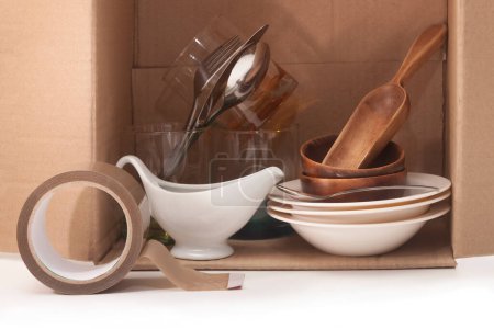 Foto de Platos de vidrio y madera, cucharas y tenedores en una caja de cartón, cinta adhesiva - Imagen libre de derechos