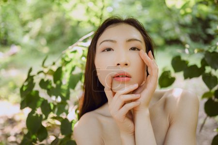 Photo for Close up outdoor portrait Beautiful young Chinese Asian woman perfect skin posing outside sunny summer day green foliage. Natural facial treatment. Cosmetology, skin care and spa. Fragnance concept - Royalty Free Image