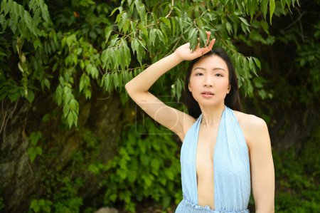 Photo for Close up outdoor portrait of Beautiful young happy Chinese Asian woman perfect skin posing outside sunny summer day green foliage. Natural facial treatment. Cosmetology, skin care and spa. - Royalty Free Image