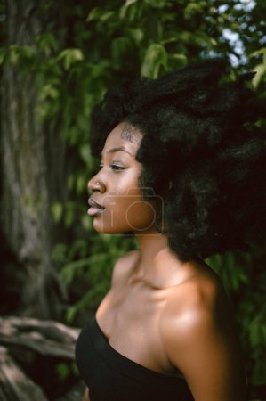 Nahaufnahme Kopfschuss Modeporträt Schöne junge Afroamerikanerin Schwarze Frau nackten Schultern posiert draußen, sonnigen Sommertag grünes Laub. Gesichtsbehandlung. Kosmetologie, perfekte Hautpflege und Wellness