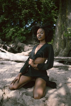 Mode Strandporträt Schöne junge Afroamerikanerin Schwarze Frau posiert draußen an der Sandküste mit großen grünen Bäumen an sonnigen Sommertagen. Kosmetologie, natürliche Hautpflege und Wellness