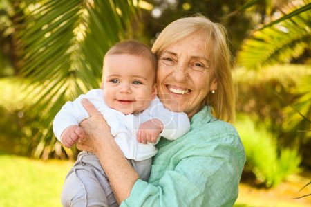 Schöne glücklich lächelnde Seniorin, die an den Händen einen niedlichen kleinen Jungen hält. Großmutter und Enkel amüsieren sich gemeinsam an einem tropischen Sommertag im Park. Familienkonzept für mehrere Generationen