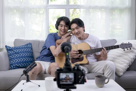 Photo for Young Asian gay couple blogger vlogger and online influencer recording musical video content playing guitar and singing at home. LGBT male couple performing and  shooting clip for social media. - Royalty Free Image