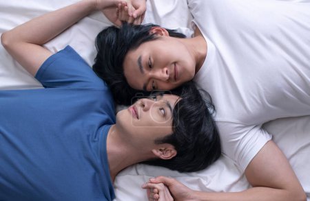 Téléchargez les photos : Vue grand angle de sourire asiatique gay couple relaxant et couché dans le lit. LGBT couple masculin concept de style de vie. - en image libre de droit
