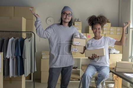 Téléchargez les photos : Confident mixed race young couple of Asian man and african-american woman retail seller, entrepreneur, online store drop shipping small business owner looking at camera in delivery shipping warehouse - en image libre de droit