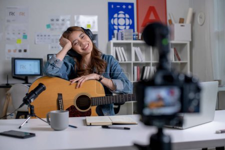Photo for Young Asian female graphic designer blogger influencer playing guitar while shooting education tutorial vlog training filming video course for social media at studio. - Royalty Free Image
