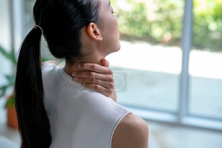 Mujer asiática tiene dolor de cuello y hombro. Mujer sosteniendo el cuello doloroso con otra mano. Personas con problemas musculares, atención médica y medicina.