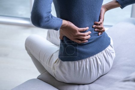 Foto de Mujer que sufre de dolor de espalda en el sofá. Mujer con dolor de espalda en casa. - Imagen libre de derechos