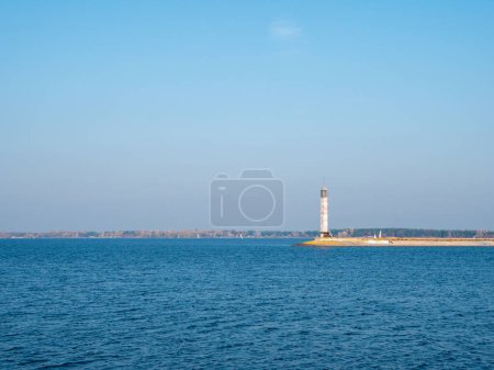 Téléchargez les photos : Vieux phare en béton sur le bord de la flèche de la mer de Kiev, eau bleue calme, ciel bleu sans nuages, et étroite bande de rive à l'horizon. - en image libre de droit