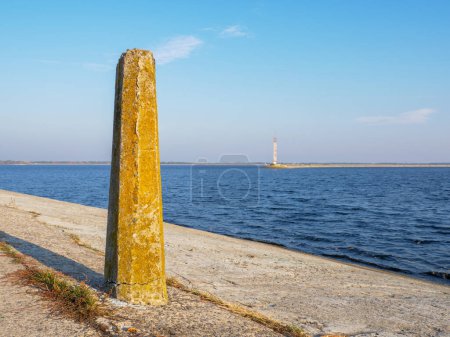 Téléchargez les photos : Vue de la borne en béton sur le vieux phare en béton sur le bord de la flèche de mer de Kiev, eau bleue calme, ciel bleu et étroite bande de rive à l'horizon. - en image libre de droit