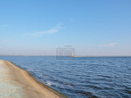 Téléchargez les photos : Vieux phare en béton sur le bord de la flèche de mer de Kiev, eau bleue calme avec yacht blanc lointain et ciel bleu avec des nuages de plumes, étroite bande de rive à l'horizon. - en image libre de droit