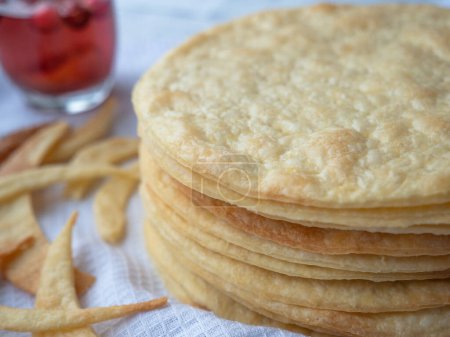 A pile of baked thin round buttery layers, dough scraps on a white waffle towel ready to make a shortcrust puff pastry Napoleon cake. A glass of red berry drink nearby.