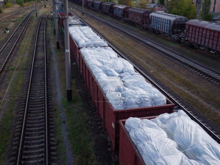 Téléchargez les photos : Un long train de marchandises avec des wagons sans toits chargés d'énormes sacs blancs et attendant à la gare de Kiev, en Ukraine. - en image libre de droit