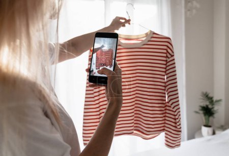 Mujer tomando fotos de camiseta a rayas en el teléfono inteligente 