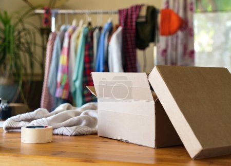 Photo for Box parcel on desk with clothes inside. Sustainable fashion, resale clothes, clothing rental - Royalty Free Image