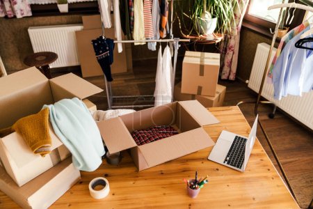 Photo for High angle view of desk with cardboard box parcel with clothes, clothes resale concept. - Royalty Free Image