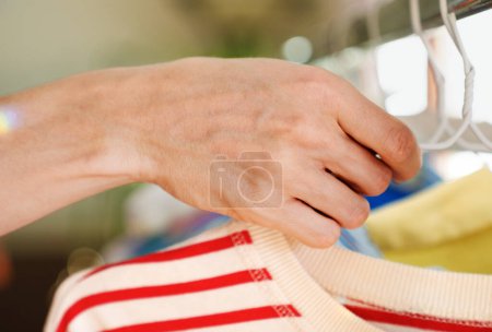 Foto de Cerca de la mano de la persona tomando camisa a rayas en la percha. ropa colgada en el carril. - Imagen libre de derechos