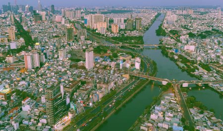 Vista aérea desde el dron de Ho Chi Minh, gran ciudad asiática con hilera de casas llenas de gente, canal Nhieu Loc Thi Nghe, puente Y que cruza el agua, tráfico de vehículos por carretera, barrio pobre de nivel 4