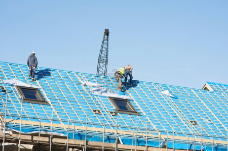 Photo for Nijmegen, Netherlands - February 8, 2023: Workers at work on a roof under construction covered with blue plastic with a clear blue sky - Royalty Free Image