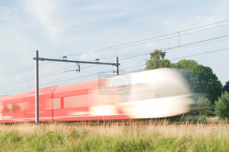 Téléchargez les photos : Le train rouge et blanc passe à grande vitesse, brouillé par une longue exposition à Arnhem aux Pays-Bas - en image libre de droit