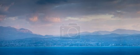Foto de Vista panorámica y tranquila del paisaje marino y las siluetas de las montañas contra el paisaje nublado durante la puesta del sol - Imagen libre de derechos