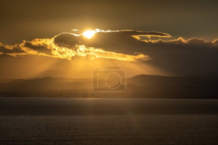 Foto de Vista panorámica de la luz del sol que fluye sobre el paisaje marino contra la silueta de la montaña y el cielo nublado durante el amanecer - Imagen libre de derechos