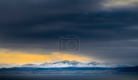 Foto de Vista idílica del paisaje marino y la cordillera nevada contra las nubes de tormenta durante el atardecer - Imagen libre de derechos