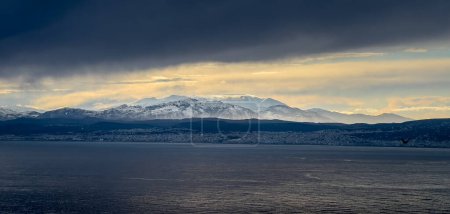 Foto de Vista idílica del paisaje marino y la cordillera nevada contra el paisaje nublado durante la puesta del sol - Imagen libre de derechos