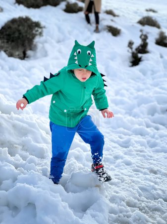 Foto de Longitud completa del niño caucásico con abrigo de invierno jugando en tierra cubierta de nieve durante las vacaciones de invierno - Imagen libre de derechos