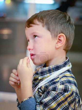 Foto de Vista lateral de lindo niño elemental caucásico mirando hacia arriba y la limpieza de la nariz con hisopo de algodón en casa - Imagen libre de derechos