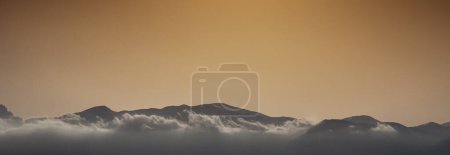 Foto de Vista panorámica panorámica de las nubes que cubren las siluetas cadenas montañosas contra el cielo durante la puesta del sol - Imagen libre de derechos