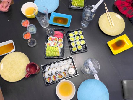 Foto de Vista de alto ángulo del delicioso sushi servido en bandejas con vasos y platos en la mesa en el restaurante - Imagen libre de derechos