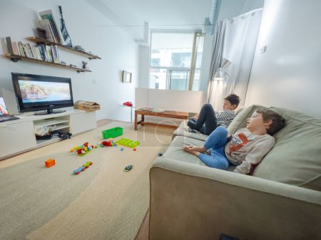 Foto de Hermanos caucásicos viendo la televisión mientras se relajan juntos en el sofá en la sala de estar en casa durante el fin de semana - Imagen libre de derechos