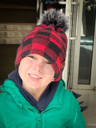 Foto de Retrato de cerca del lindo niño caucásico con sombrero de punto y abrigo de invierno contra la estructura construida - Imagen libre de derechos