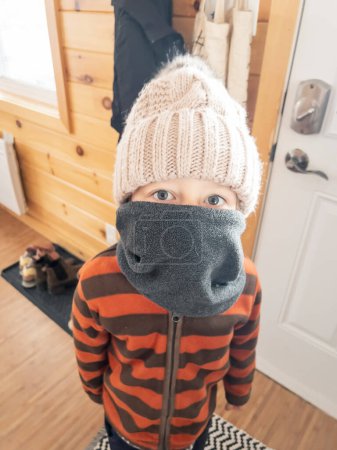 Foto de Retrato de primer plano del niño caucásico cubriendo la cara con ropa de abrigo mientras está de pie en casa - Imagen libre de derechos