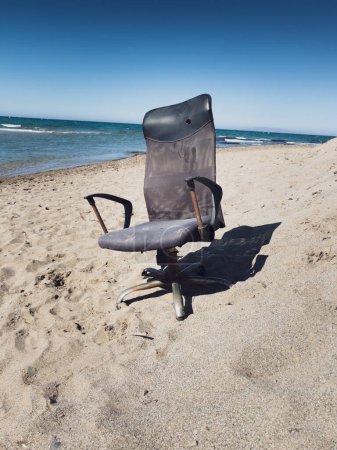 Foto de Silla de oficina vacía abandonada en la playa de arena contra el paisaje marino y el cielo azul claro en un día soleado - Imagen libre de derechos