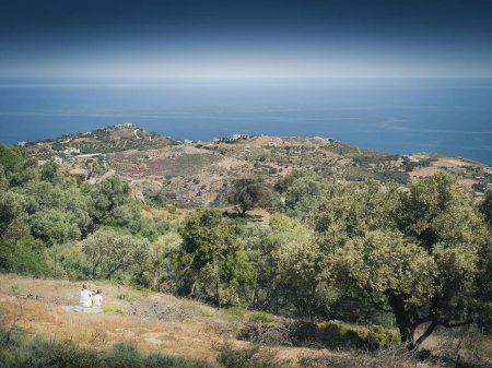 Photo for Mother and son looking at seascape against clear blue sky while sitting on lush mountain during summer - Royalty Free Image