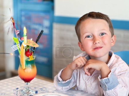Foto de Primer plano retrato de lindo chico caucásico con mocktail en la mesa haciendo cara mientras está sentado en el restaurante - Imagen libre de derechos