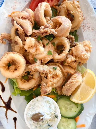 Foto de Directamente encima de primer plano de los anillos de calamares fritos servidos con salsa y ensalada en plato - Imagen libre de derechos