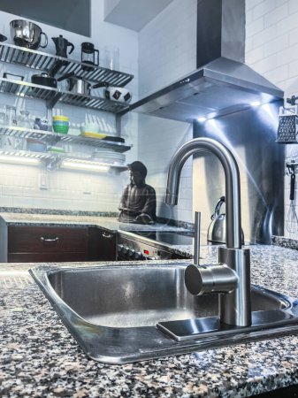 Foto de Grifo de acero con fregadero en la isla de la cocina y estatuilla de buddha sobre encimera en la cocina moderna en el hogar - Imagen libre de derechos